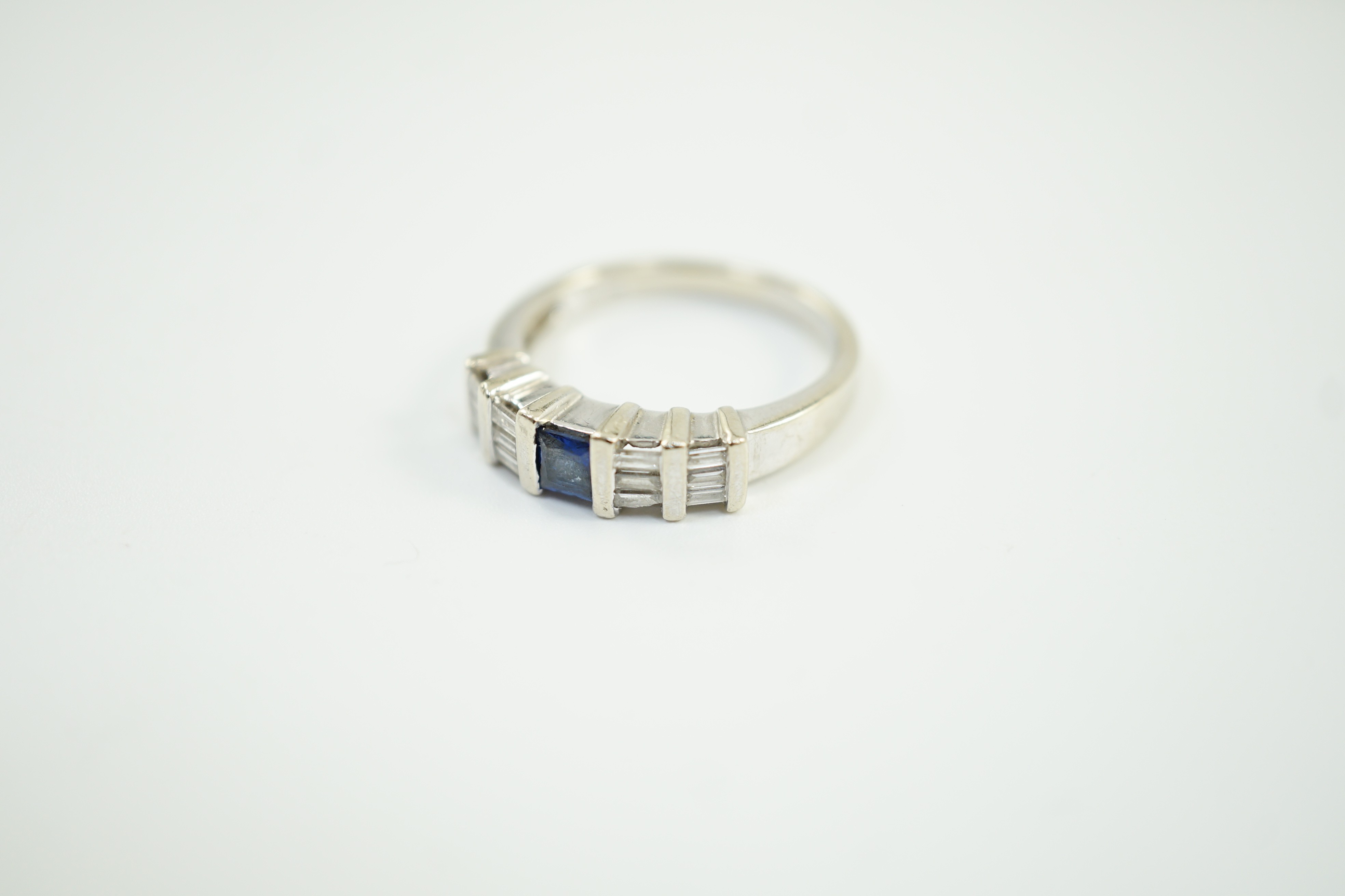 A modern 585 white metal, single stone sapphire and twelve stone baguette cut diamond cluster set half hoop ring, size N/O, gross weight 4 grams.